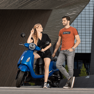 Man lachend naar een poserende vrouw op blauwe scooter voor Rotterdam Centraal